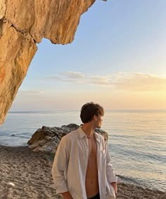 a man standing on top of a sandy beach next to the ocean under a cliff