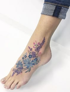 a woman's foot with blue and purple flowers on the bottom of her leg