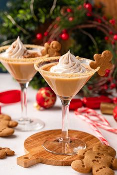 two glasses filled with dessert on top of a wooden cutting board next to christmas decorations