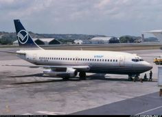 an airplane is parked on the tarmac with people standing around it and another plane in the background