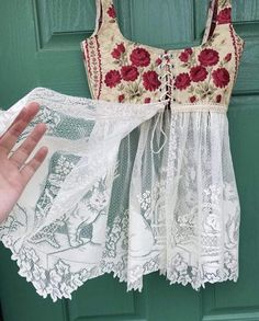 a hand is holding up a piece of white lace with red flowers on it, next to a green door