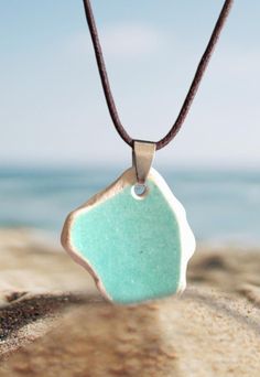 a blue and white pendant on a brown cord at the beach with water in the background