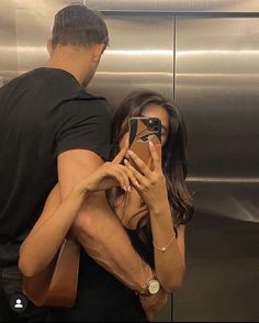 a man and woman standing in front of an elevator taking pictures with their cell phones