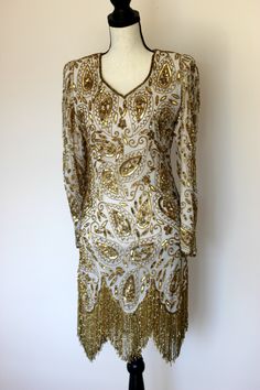 "Beautiful Gunit Flapper Dress with Gold beads and sequins throughout. Excellent condition! Long flowy gold beaded fringe. This one is a true head turner!! Zipper in the back Measuring: 36\" long 34\" bust 28\" waist 34\" hip 23\" sleeve Beautiful! in every way!! Pet free/ smoke free Enjoy!" Festive Gold Hand Embellished Dress, Festive Gold Hand-embellished Dress, Glamorous Festive Dress With Gold Embroidery, Elegant Wedding Flapper Dress With Rhinestone Fringe, Elegant Fitted Flapper Dress For Festive Occasions, Formal Sequined Flapper Dress For Party Season, Glamorous Sequined Flapper Dress For Formal Occasions, Gold Embellished Long Sleeve Sequin Dress, Glamorous Gold Embroidered Festive Dresses