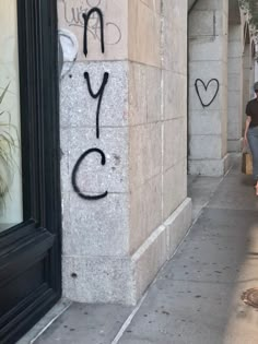 a woman walking down a sidewalk past a tall building with graffiti on it's side