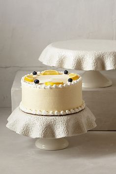 two tiered cake with white frosting and blueberries on top sitting on pedestals