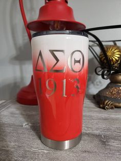 a red and white coffee cup sitting on top of a table next to a lamp