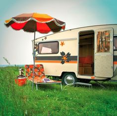 an old camper is parked in the grass with its door open and chairs underneath it