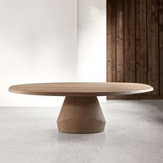 a round wooden table sitting on top of a white floor next to a wall with wood paneling