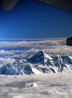 the view from an airplane window looking at snow covered mountains in the distance and clouds below