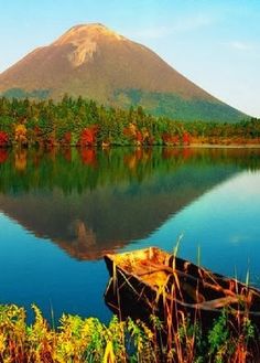 a boat sitting on top of a lake next to a mountain covered in trees and foliage