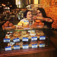 two women standing in front of a display case filled with donuts and pastries