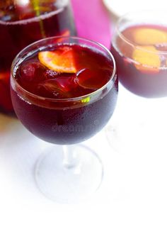 two glasses filled with red liquid and orange slices on top of each glass, next to another