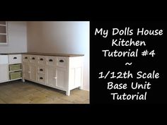 an image of a kitchen with white cabinets and wood flooring in the background is a black sign that says my dolls house kitchen