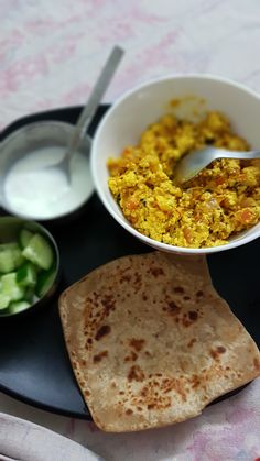 a plate with some food on it next to a bowl of yogurt and cucumbers