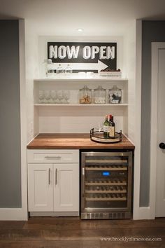 an open wine rack in the corner of a kitchen with white cabinets and wood counter tops