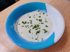 a blue bowl filled with white sauce and parsley on top of a wooden table