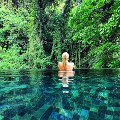 a woman sitting in the middle of a swimming pool surrounded by trees and greenery