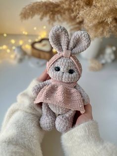 a crocheted bunny is held up by someone's hand in front of a christmas tree