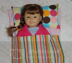 a doll laying on top of a pillow with a pink shirt and colorful striped skirt