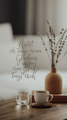 a cup of coffee sitting on top of a wooden table next to a vase filled with flowers