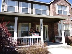 a group of people standing on the front porch of a house with a for sale sign