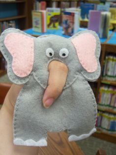 an elephant puppet is being held up by someone's hand in front of bookshelves