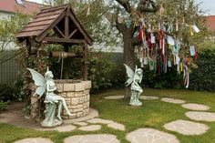 two fairy statues sitting in the grass next to a stone wall and tree with streamers hanging from it