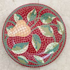 a red and green mosaic plate with leaves on the bottom, sitting on a white marble floor