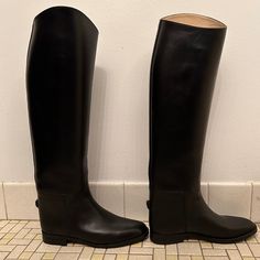 two tall black boots sitting on top of a tiled floor next to a white wall