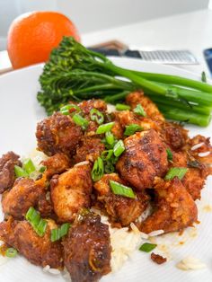 a white plate topped with meat and veggies next to an orange on a table