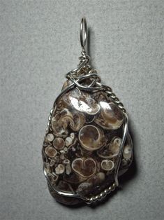 Turritella Agate Pendant Wire Wrapped in .925 Sterling Silver Round Wire This interesting stone is a combination of fossilized turritella (snail) shells in a rich brown agate. It is best worn with “interesting” clothing, patterned after the natural world: leaves, flowers, shells, etc. Color wise, it works well with earth tone colors, and quite well with most colors, but better with darker than lighter. Description: Fossilized turritella snail shells in a brown agate backgroun; rounded triangular Artisan Brown Jewelry With Natural Inclusions, Unique Brown Shell Jewelry, Unique Brown Spiral Jewelry, Shell Fossil, Turritella Agate, Interesting Clothing, Brown Agate, Earth Tone Colors, Snail Shell