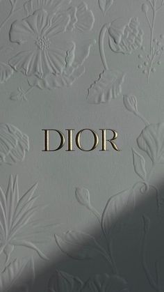 the word dior is written in gold on a white wall with floral designs and leaves