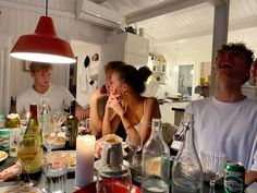 a group of people sitting around a table with bottles and glasses on it, all looking up