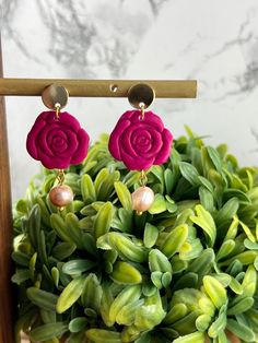 the pink rose earrings are on display in front of some green plants with pearls hanging from them