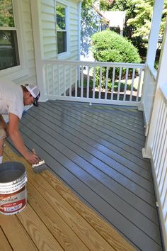 a man painting the outside of a house with gray paint on it's deck