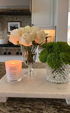 candles and flowers on a counter top in a kitchen with white cabinets, granite counters and stainless steel appliances