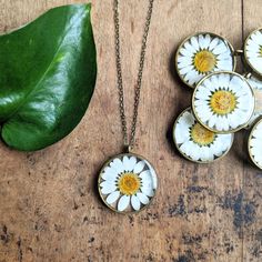 four necklaces with daisies on them sitting next to a green leaf and plant