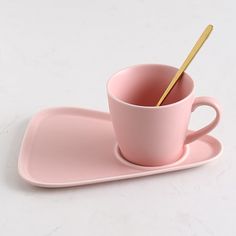 a pink coffee cup and saucer with a gold spoon on a white table top