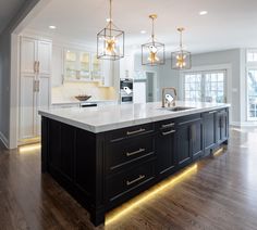 a large kitchen with an island in the middle and lights hanging from it's ceiling