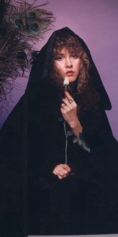 a woman wearing a black robe and holding a rose in her hand with a purple background