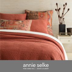 an orange bedspread and pillows in a bedroom with white walls, wood flooring and decorative vases