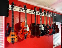 a red wall with guitars hanging from it's sides and on the wall is a guitar rack