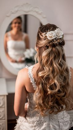 a woman in a wedding dress looking at herself in the mirror with flowers in her hair