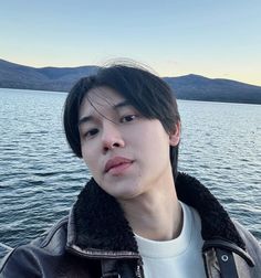 a young man standing on top of a boat next to the ocean with mountains in the background