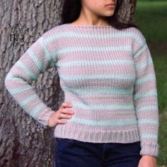 a woman standing in front of a tree wearing a pink and blue striped knit sweater