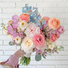 a person holding a bouquet of flowers in front of a white brick wall with blue and pink flowers