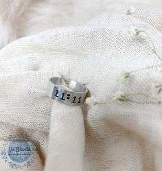 a silver ring with the number 11 11 on it sitting on a white blanket next to flowers