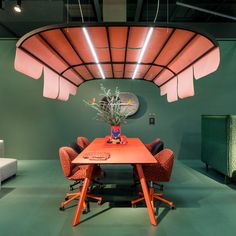 an orange table surrounded by red chairs in a room with green walls and flooring