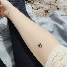 a person with a small clover tattoo on their left arm, sitting in the sand